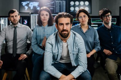 Stock trader teamwork looking at camera against multiple monitors
